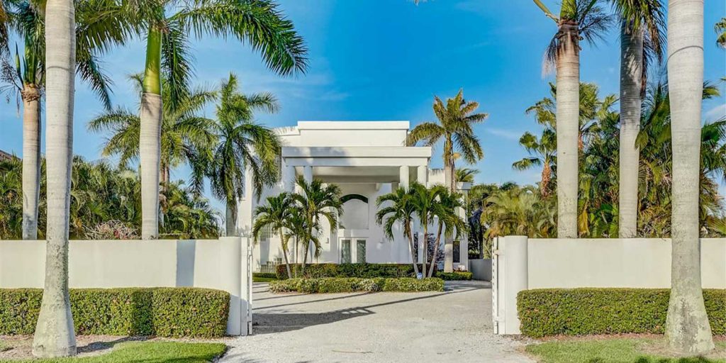 A photo of a large white 2-story historic home located behind a concrete wall in one of Longboat Key's historic neighborhoods