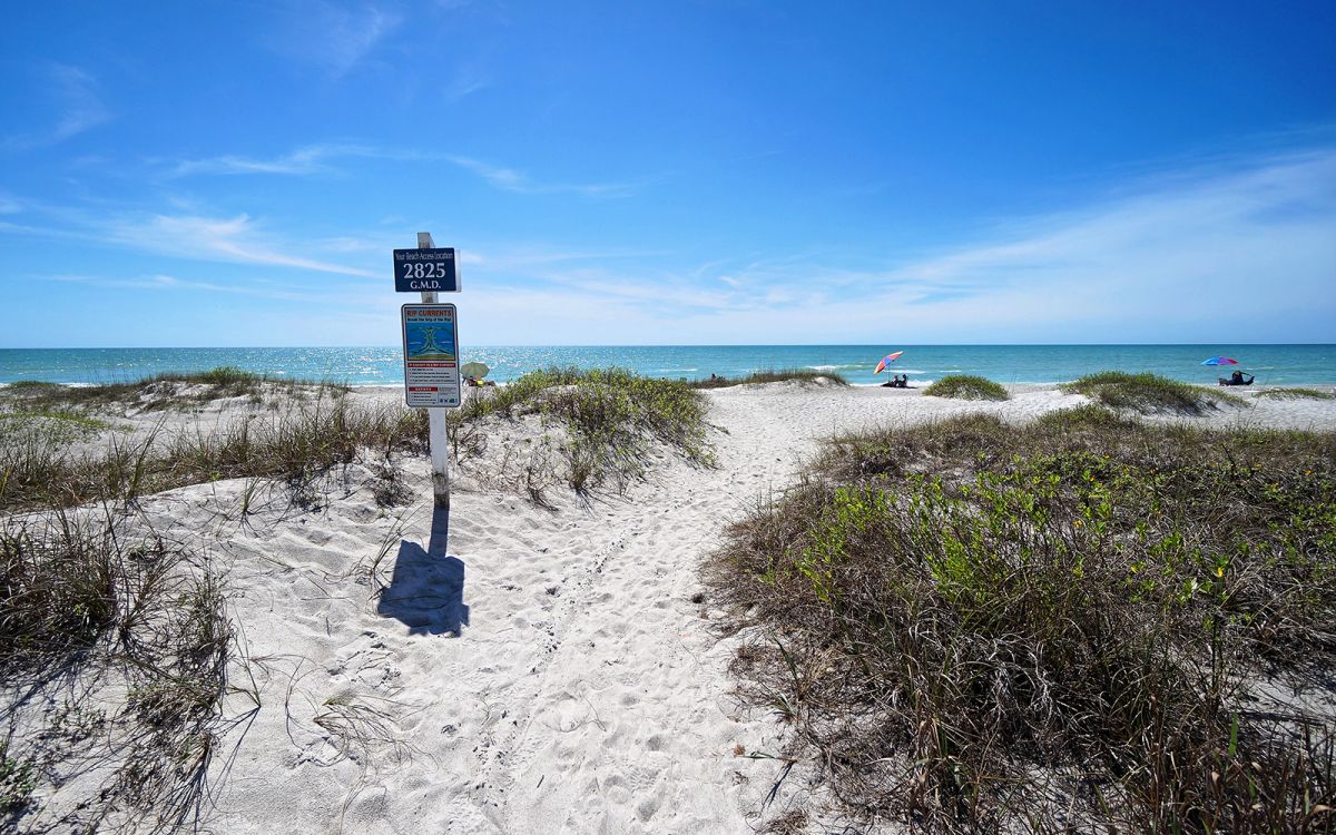 Small blue sing on white post sitting along beach sand path to the Gulf of Mexico