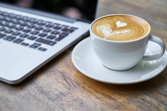 cup of coffee sitting on a wood table next to a laptop