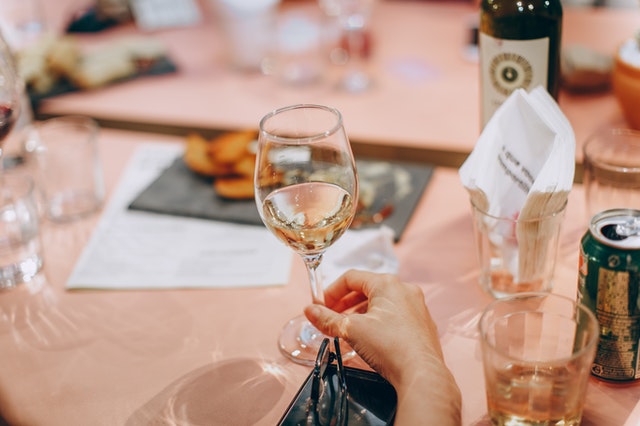 a tabe with pink table cloth and hands holding a glass of white wine