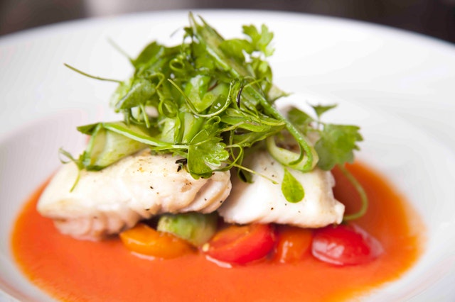 A fancy vegetable medley with red broth topped with white fish and arugula