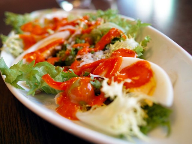 an oval white plate with an arugula base, and tomato's topped with mozzarella and thin sliced roasted red peppers.