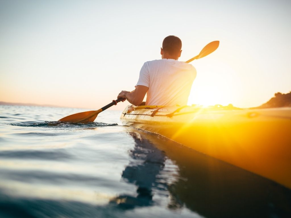 The back side of a man in a white shirt holding a paddle while Kayaking Longboat Key Florida 