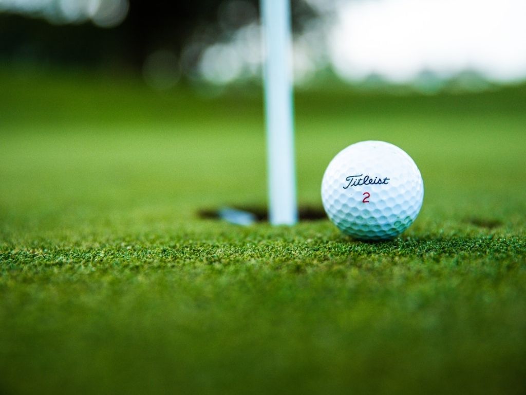 A close up photo of a golf ball sitting next to a hole on the golf course.