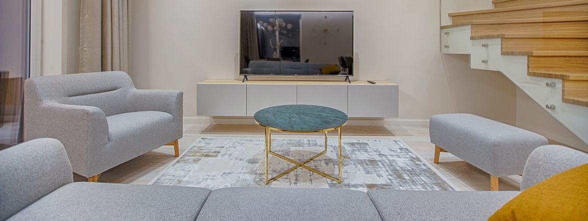 This photo shows an idea for furniture decorating and layout. The tv is the focal point so a gray sofa faces the TV wall. A coffee table is in front of the sofa.  To the left of the table is a gray chair. To the right is an gray fabric ottoman/bench. 