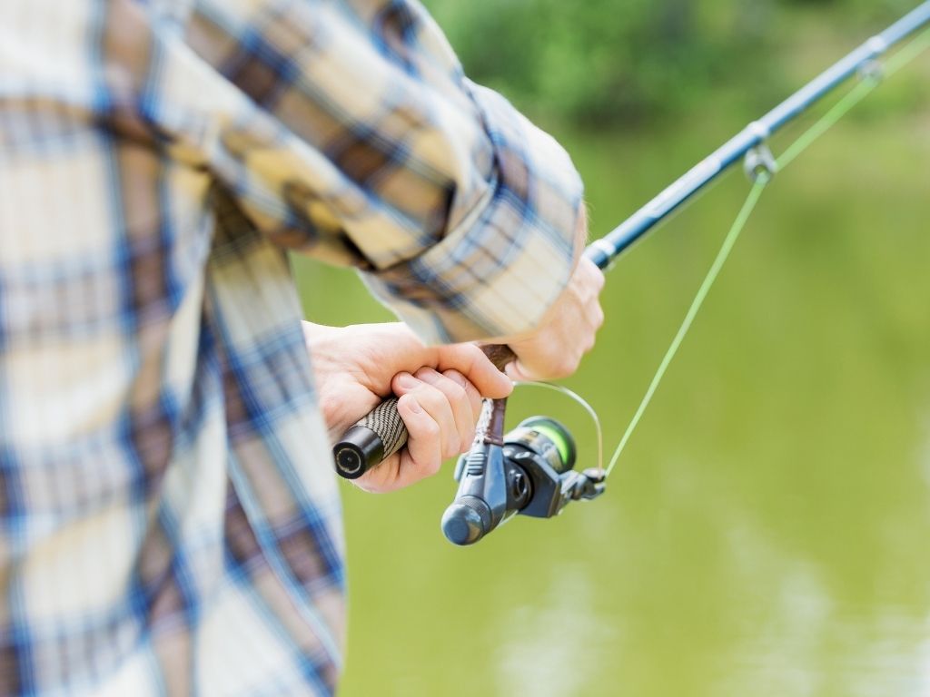 A close up of a mans arm wearing a plaid shirt holding a fishing rod.