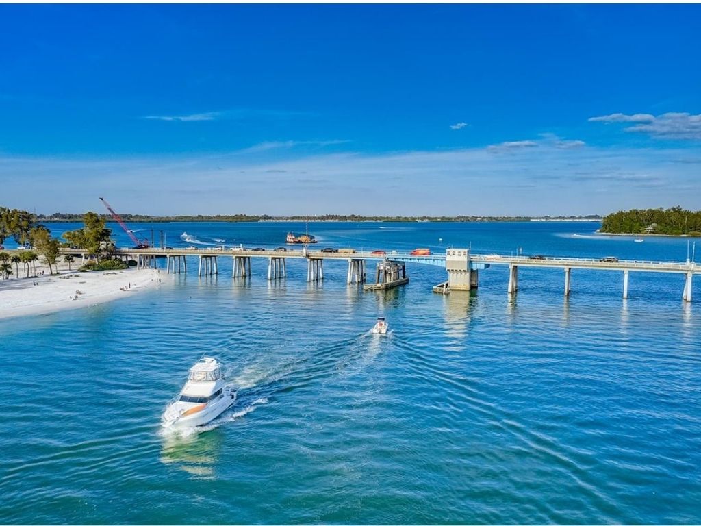 A boat on the blue-green waters of the Gulf of Mexico water with the Longpass Bridge behind it.