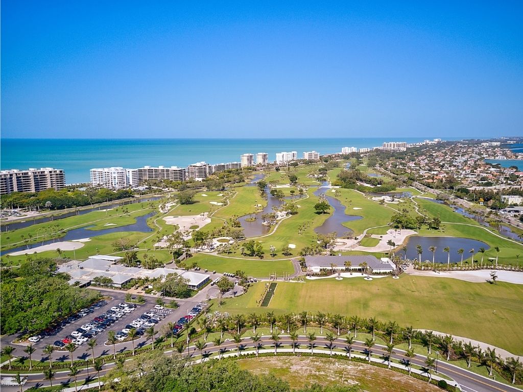 An aerial photo of The Longboat Key Club Resort showing the tennis courts, the golf course. To the left are the sparkling blue waters of the Gulf of Mexico. 