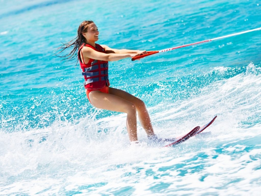This photo is an example of things to do in Longboat Key. It shows a girl with shoulder length hair wearing a red life vest on water ski's.