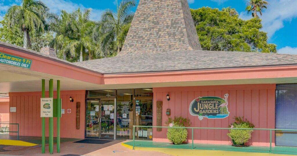 A bright salmon color building that looks like a converted gas station with a green jungle gardens sign