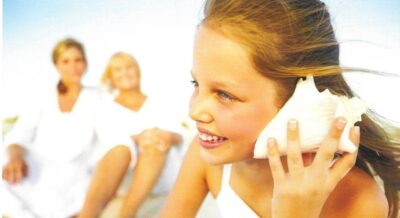 A young girl with her ear to a seashell enjoying her time within one of the many Longboat Key neighborhoods. 