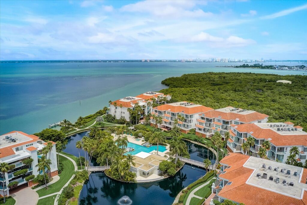 An aerial view of Tangerine Bay Club showing ten tan buildings with terra cotta roof tiles that wrap around the community amenities.